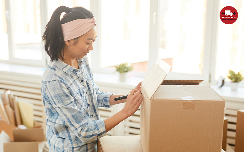 Asian Woman Writing On Cardboard Box Labelling For Moving Out To New House