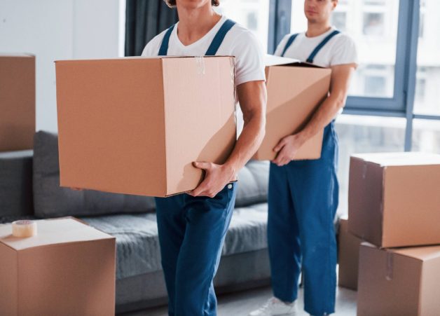 with-boxes-hands-two-young-movers-blue-uniform-working-indoors-room-min (1)